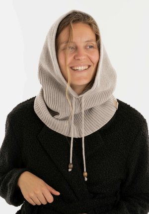 Beige gebreide sjaal met capuchon, voorzien van een ribbelstructuur, verstelbare trekkoorden en houten kralenaccenten, gedragen over een zwarte gestructureerde jas.