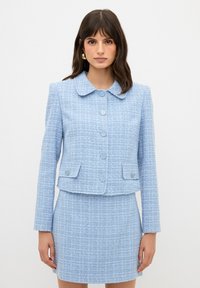 Giacca in tweed azzurro chiaro con colletto arrotondato, cinque bottoni e due tasche frontali, abbinata a una gonna mini coordinata. Tessuto testurizzato.