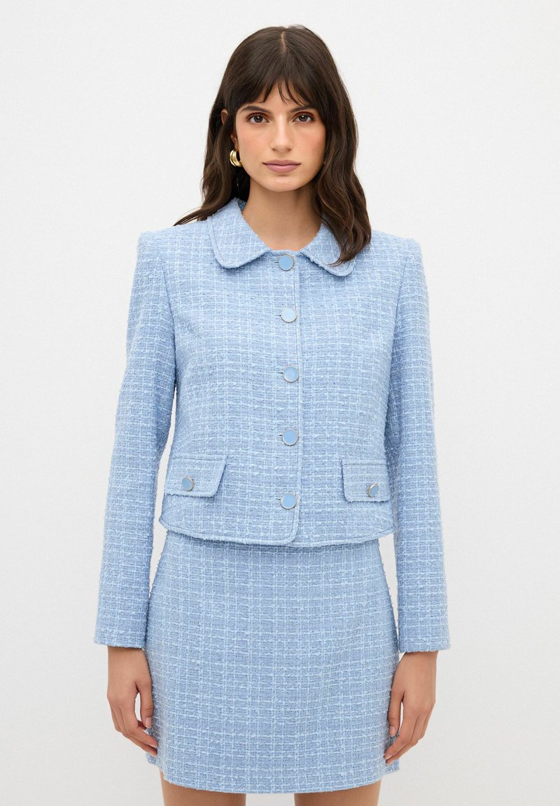 Giacca in tweed azzurro chiaro con colletto arrotondato, cinque bottoni e due tasche frontali, abbinata a una gonna mini coordinata. Tessuto testurizzato.