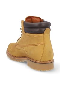 Bota de tobillo de cuero marrón con un cuello acolchado, cuerpo amarillo, suela texturizada y ojales de metal para los cordones, que muestra un diseño robusto.