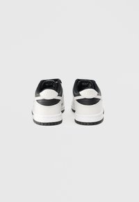 Nike tenisky z belo usnjeno podlago, črnimi detajli in oblazinjenim ovratnikom. Zadnji del vključuje logotip in teksturirano peto.