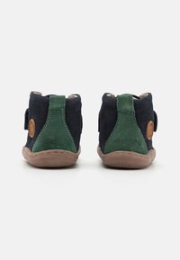 Botas de tornozelo em camurça azul e verde com solas de borracha bege e um emblema castanho, apresentando uma faixa de velcro para ajustes fáceis.