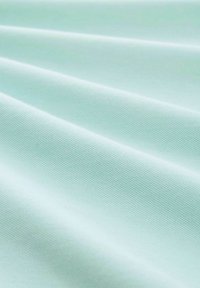 Helles mintgrünes Gewebe mit einer glatten Textur, das subtile gerippte Muster und Falten aufweist und eine weiche, flexible Drapierung zeigt.