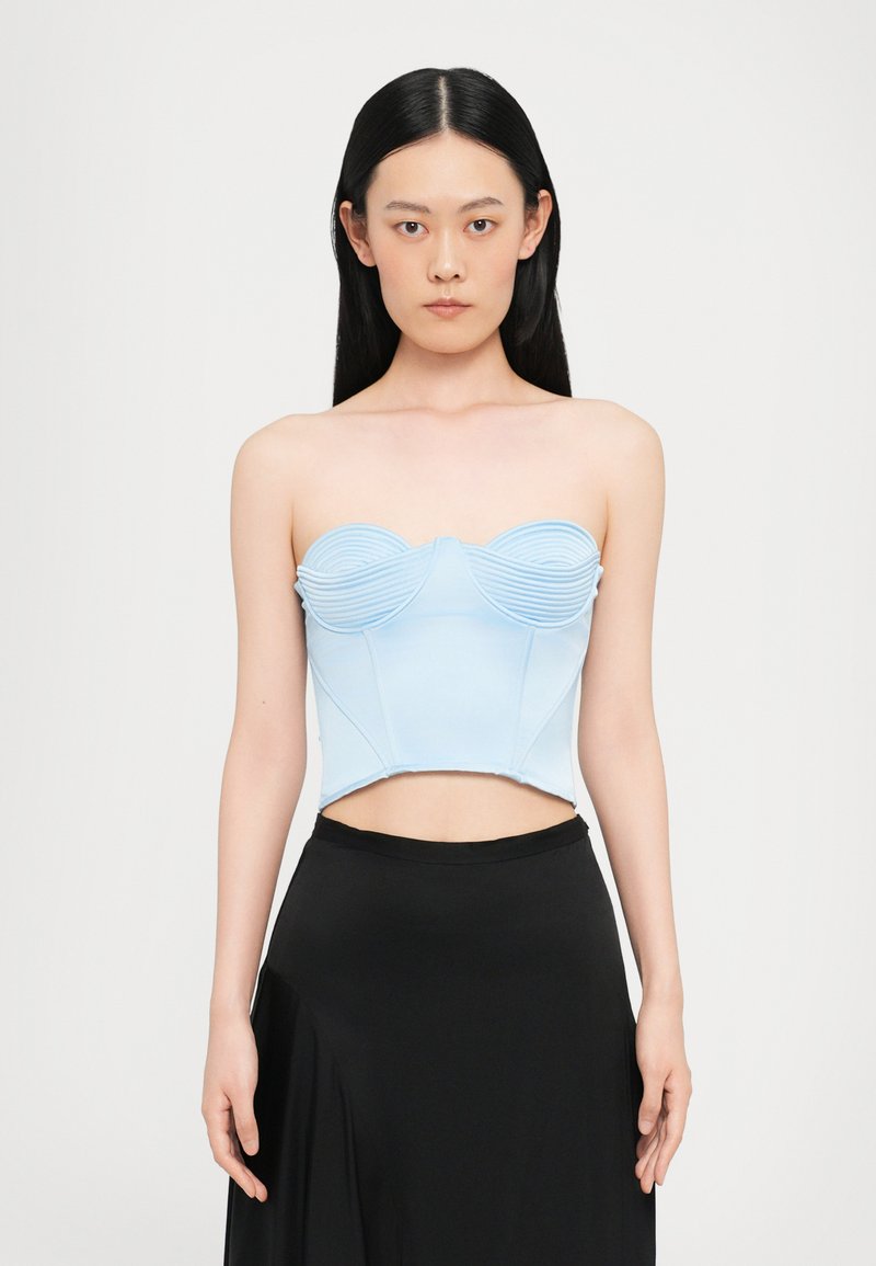 Top sin mangas de color azul claro con detalles acanalados, copas contorneadas y un diseño corto, combinado con una falda negra de cintura alta. Textura suave.