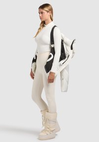 Hvid langærmet bluse, cremefarvede leggings og knæhøje hvide støvler. Sort og hvid puffy jakke over skulderen. Glat tekstur, tætsiddende design.