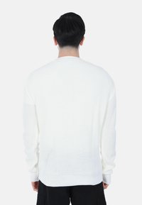 Maglione bianco lavorato a maglia con un motivo testurizzato, scollo rotondo e maniche lunghe, mostrato da dietro.