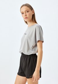 Grå mesh kortærmet skjorte med teksten "GOOD BEAR", parret med sorte shorts med elastisk talje, der har en løs pasform og en glat tekstur.