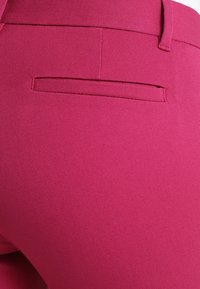 Pantalon ajusté en tissu rose vif avec une surface texturée. Dispose d'une poche arrière unique, mettant en valeur des lignes épurées et une conception sur mesure.