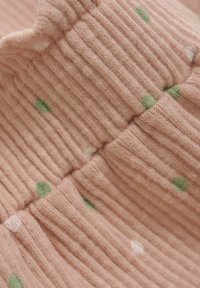 Texturerad bomullstyg i mjuk persikofärg med ribbning. Har gröna och vita prickar. Slät känsla med lätt stretch.