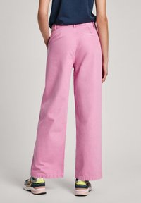 Jeans rosa de perna larga com uma textura suave e um ajuste casual. Bolso traseiro visível, combinados com sapatos atléticos multicoloridos.