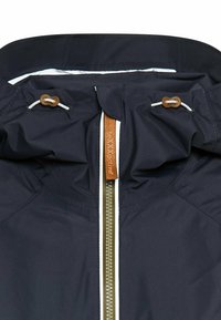 Marineblauwe waterdichte jas met een hoge kraag, een dubbele rits met lichtgekleurde afwerking en bruine toggles voor aanpassing. Gladde textuur.