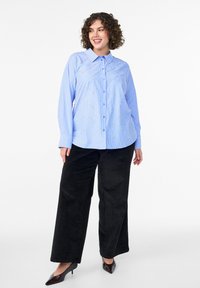 Light blue button-up shirt with a collar, featuring a striped pattern and decorative stitching. Paired with black wide-leg pants and heels.
