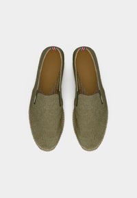 Ζευγάρι από χακί ελιάς παντόφλες καμβά με καφέ εσωτερικά πέλματα και μικρή λεπτομέρεια από ύφασμα κόκκινο, λευκό και μπλε στην ταμπέλα της φτέρνας.