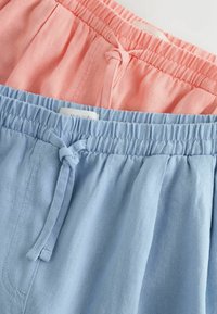 Deux shorts à taille élastique avec cordons, un bleu clair et un corail rose, présentés pliés et superposés sur un fond blanc.