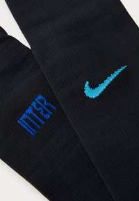 Černé sportovní ponožky s modrým logem "INTER" na jedné straně a tyrkysovým logem Nike na straně druhé, vyrobené z texturovaného pleteného materiálu.
