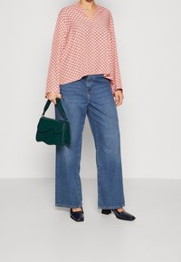 Red patterned blouse with a v-neck, paired with wide-leg blue jeans and a green textured handbag. Black square-toed heeled shoes complete the look.