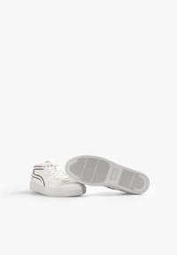 Sneaker alte bianche in tela con suola in gomma, caratterizzate da un design a linee nere contrastanti e un motivo testurizzato sulla suola.