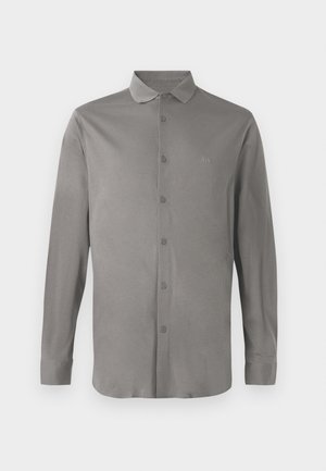 Szary longsleeve z gładkiego materiału, z zapięciem na guziki z przodu, klasycznym kołnierzykiem i subtelnym haftowanym logo na klatce piersiowej.