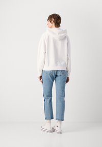 Felpa bianca con cappuccio e vestibilità comoda, abbinata a jeans azzurri a gamba dritta e sneaker bianchi con dettagli neri.