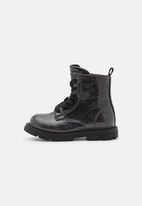 Botas de tobillo negras con purpurina, punta redonda, superficie de charol texturizada, seis ojales y cordones negros. Presenta un tirador en forma de bucle en el talón y una suela gruesa.