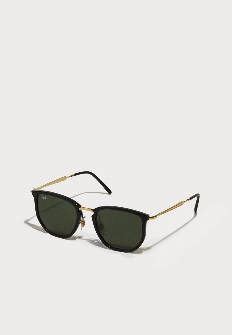 Ochelari de soare negri, tip cat-eye, cu lentile verzi, accente din metal auriu și brațe negre subțiri. Rama texturată cu un design îndrăzneț și geometric.