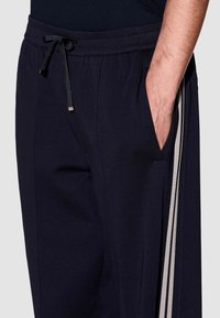 Navy blue trainingsbroek met elastische tailleband en koord, voorzien van zijzakken en contrasterende verticale strepen langs de benen.