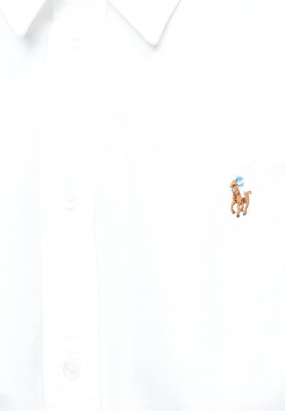 Fehér inggalléros ing gombokkal és a mellrészen egy kis hímzett barna ló, amely kék kalapot visel.