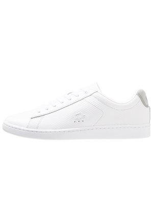 White low-top sneaker with lace-up front, minimal stitching, textured side panel, and embossed crocodile logo on the side.