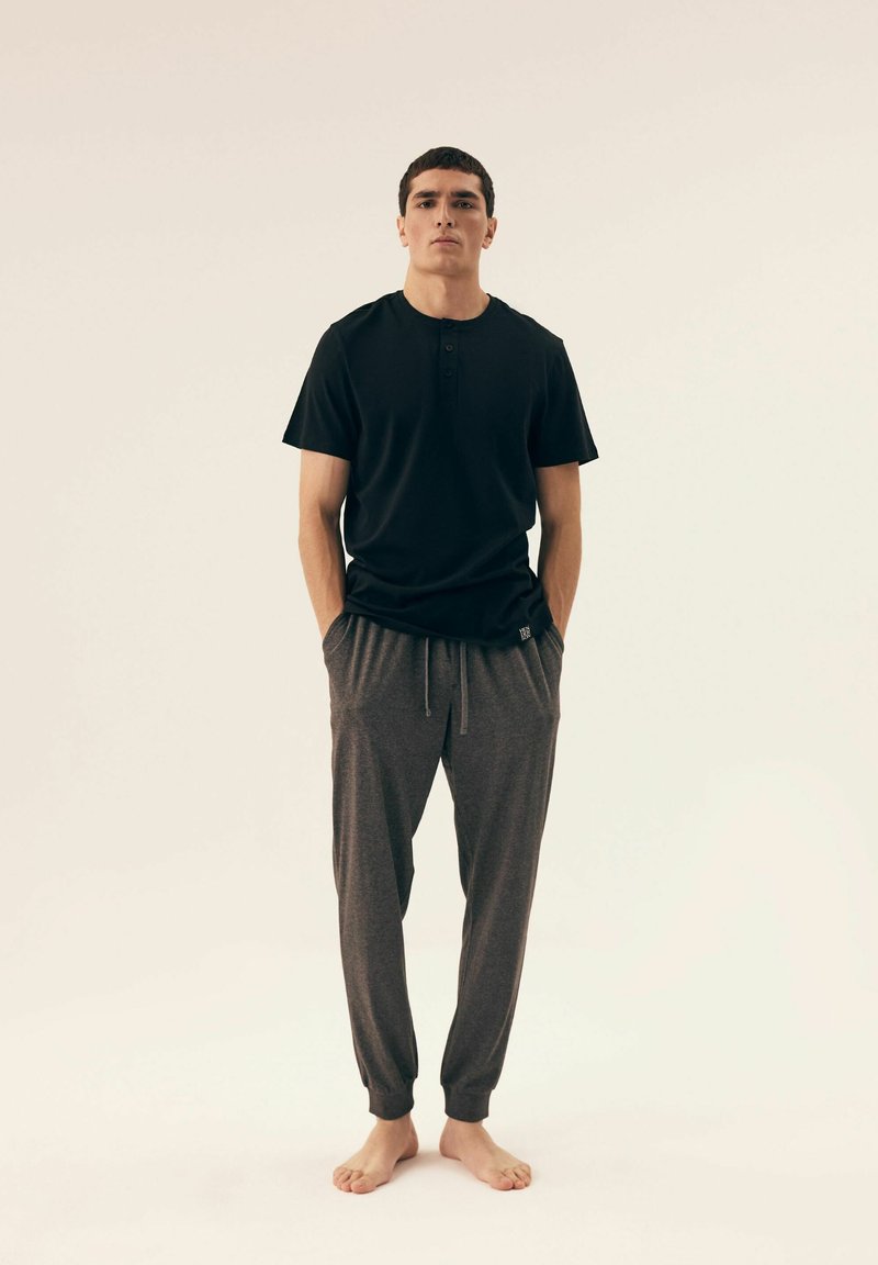 Black short-sleeve henley shirt with three buttons, paired with gray, tapered sweatpants featuring an elastic waistband and cuffs.
