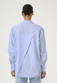 Camicia a righe azzurro chiaro con colletto a punta, maniche lunghe e un design unico sul retro con spacco asimmetrico. Il tessuto è morbido e leggero.