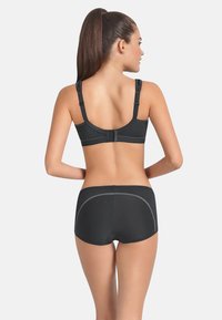Sujeción deportiva negra y pantalones cortos a juego con un diseño texturizado y un ribete a contraste. Tirantes ajustables y cierre de gancho en la parte trasera.
