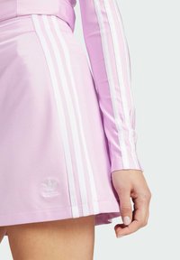 Vestido deportivo rosa con franjas laterales blancas, una silueta ajustada y un logo bordado de Adidas cerca del dobladillo. Textura de tela suave.