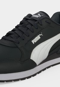 Μαύρο sneaker Puma με λευκή λωρίδα στο πλάι, μαύρα κορδόνια και λογότυπο Puma στη γλώσσα και στο πλάι, απεικονίζεται από κοντινή λοξή γωνία.