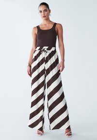 Brown ribbed tank top paired with wide-leg, striped pants in brown and cream. Features an elastic waistband with a drawstring. Smooth fabric.