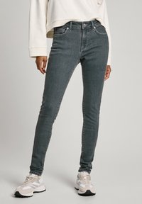 Vaqueros ajustados grises con una cintura de media altura, cinco bolsillos y detalles de costura sutiles, combinados con zapatillas beiges y blancas.