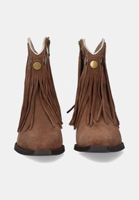 Botas de tobillo de ante marrón con detalles de flecos, cierre de cremallera y acentos metálicos en forma de círculo. Suela plana con un diseño minimalista.