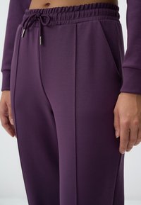 Paarse joggingsbroek van zacht materiaal, met een trekkoord in de taille, zijzakken en een gladde textuur met subtiele naaddetails.