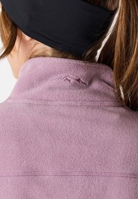 Vaaleanlila fleece-takki, jossa on korkea kaulus ja näkyvät saumat. Takissa on hienovarainen brodeerattu kuvio takakauluksessa.