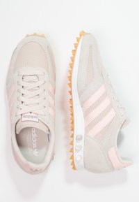 Béžové sportovní boty s růžovými akcenty, z materiálů síťovina a semiš, zaoblenou špičkou, gumovou podrážkou s hroty a logem se třemi pruhy po stranách.