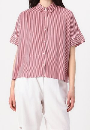 Kobieta nosząca koszulę z krótkim rękawem w pionowe czerwono-białe paski oraz białe spodnie z wysokim stanem.