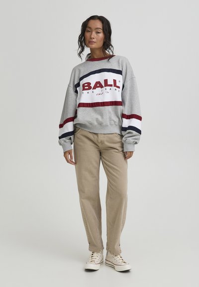 Sweat-shirt gris avec de larges rayures rouges et bleu marine, arborant le logo "BALL" ; accompagné d'un pantalon beige et de baskets blanches. Design simple et coupe décontractée.