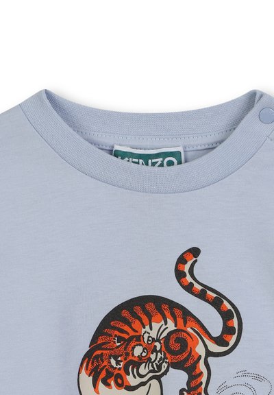 T-shirt en coton bleu clair avec col rond, arborant un graphique d'un tigre orange et noir imprimé sur le devant. Fermeture à boutons-pression.