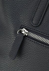 Primo piano di una borsa in pelle blu navy con texture, dotata di zip visibile, hardware argentato e un dettaglio della tracolla piatta. La superficie presenta una finitura a pelle di pesca.