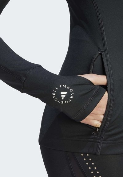 Camiseta atlética negra de manga larga con agujeros para los pulgares, que cuenta con un bolsillo con cremallera y detalles de logo en la muñeca. Tejido suave y elástico.
