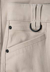 Beige tkaninová kapsa s černými nýty a přišitým černým D-kroužkem připevněným k dvojitým poutkům na opasek.