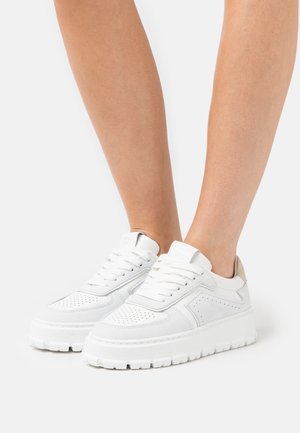 White sneakers with a textured finish, featuring perforations, thick rubber sole, and light gray accents on the heel and tongue.