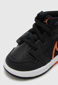 Sneaker neri con tomaia in pelle texturizzata, logo arancione, collo imbottito e suola in gomma bianca. Presenta un sistema di allacciatura con punta perforata.