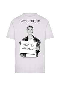 Weißes T-Shirt mit einem schwarz-weißen Grafikdesign einer Person, die ein Schild mit der Aufschrift "WAS BEDEUTEST DU?" hält, sowie Text darüber.