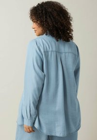 Camicia azzurro chiaro a maniche lunghe realizzata in tessuto morbido. Presenta una vestibilità comoda, polsini plissettati e un orlo dritto con dettaglio sulla spalla posteriore.