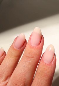 Una mano con unghie curate che presentano una sfumatura dal rosa chiaro alla base a un nude delicato sulle punte, texture liscia e forma arrotondata.